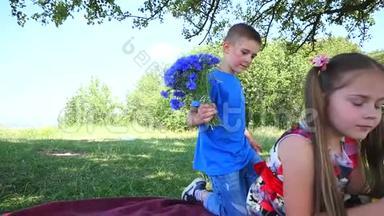 男孩正在给漂亮的女孩送花。 恋爱中的年轻夫妇。 阳光公园里两个可爱的孩子。 绿色的快乐